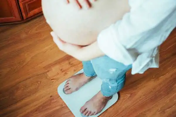 Image of woman weighing herself and experiencing weight gain through pregnancy Llanelli